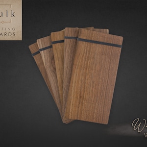 May include: A stack of six walnut wood cutting boards with black elastic bands. The boards are arranged in a fan shape and have a natural wood grain pattern. The text "Bulk Cutting Boards" is visible in the top left corner of the image. The text "Walnut Wood" is visible in the bottom right corner of the image.