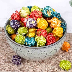 May include: A bowl filled with colorful popcorn kernels in shades of blue, green, yellow, red, and purple. The popcorn is in a gray bowl with a speckled pattern.