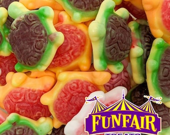 May include: A close-up of colorful gummy candies shaped like turtles. The candies are a mix of red, orange, green, and brown. The image includes the text "FUNFAIR TREATS HAND CRAFTED IN SMALL BATCHES" in a purple and yellow logo.