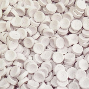 May include: A close-up image of a large pile of white round candy. The candy is smooth and has a slightly textured surface.