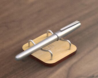 May include: A silver pen resting in a wooden pen holder with the word "oom" engraved on the holder.