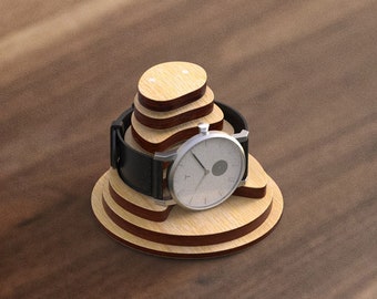 May include: A wooden watch stand with a layered design, featuring a silver watch with a black leather strap.