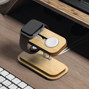 May include: A wooden charging stand for an Apple Watch and AirPods. The stand is made of light brown wood and has a black Apple Watch charging puck and a white AirPods charging puck. The stand is on a wooden desk with a white keyboard.