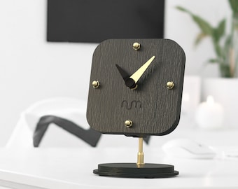 May include: A black wooden clock with gold accents and a simple design. The clock has a black face with gold hands and a gold rim. The clock is on a black stand.