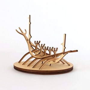 May include: A wooden model of a Viking ship with intricate details. The ship is made of light brown wood and has a rounded hull with a pointed bow and stern. The ship has a single mast and a sail, and there are several oars on each side. The ship is sitting on a wooden base.