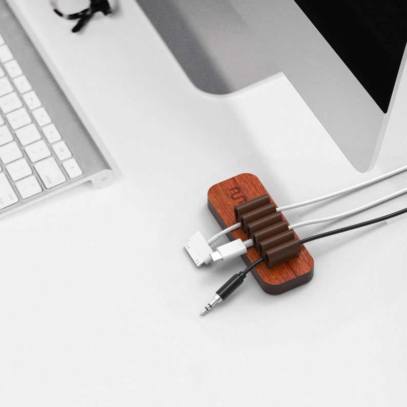 May include: A wooden cable organizer with six slots to hold cords and wires. The organizer is brown with a natural wood finish and has the word "run" printed on it.