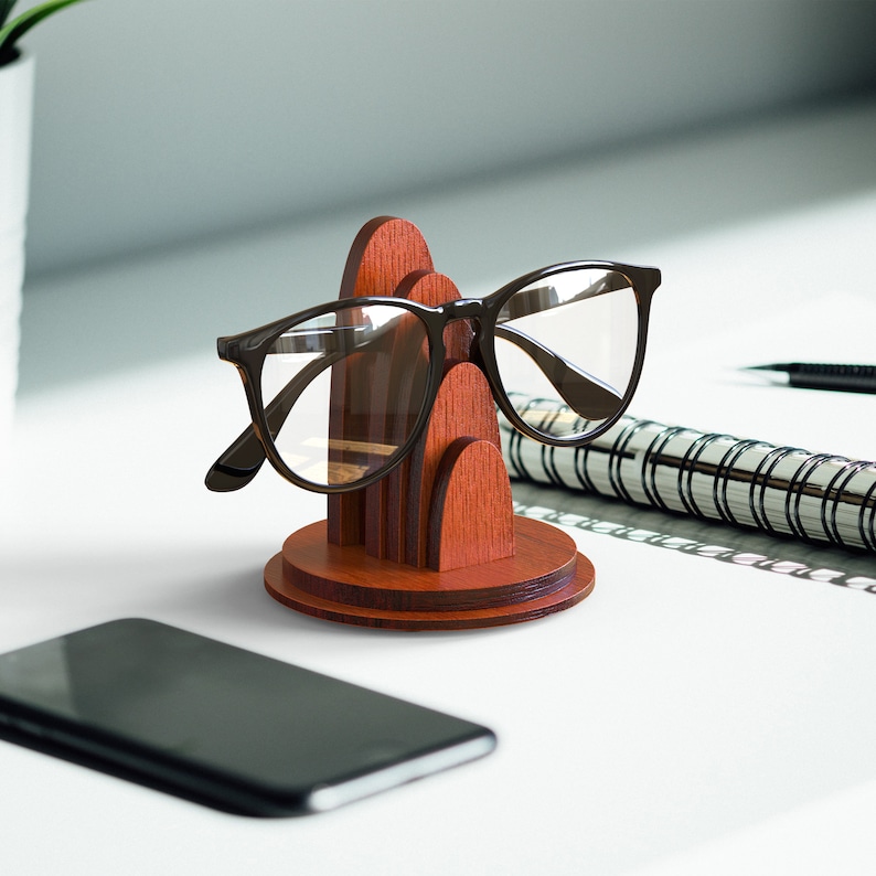 May include: A wooden glasses holder with a modern design. The holder is made of dark wood and has a rounded shape. It is designed to hold eyeglasses or sunglasses.