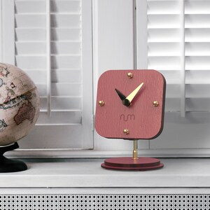 May include: A pink wooden desk clock with gold accents and black hands. The clock face has the letters "rm" in the center.