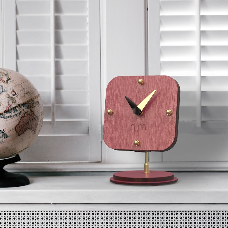 May include: A pink wooden desk clock with gold accents and black hands. The clock face has the letters "rm" in the center.