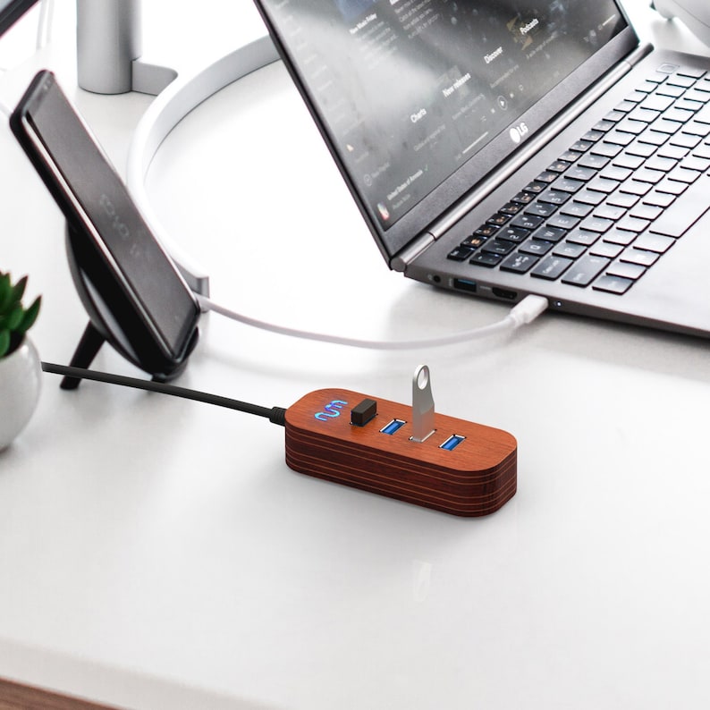 May include: A wooden USB hub with four ports and a blue LED light. The hub is connected to a laptop computer with a white cable.