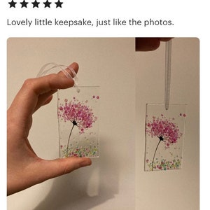 K&ouml;nnte beinhalten: Zwei kleine rechteckige Glas-Schmuckst&uuml;cke aus Fusing mit einem rosafarbenen Blumendesign und einem wei&szlig;en Band zum Aufh&auml;ngen. Die Schmuckst&uuml;cke werden in einer Hand gehalten.