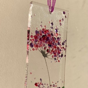 K&ouml;nnte beinhalten: Ein Glasornament mit einem lila und pinkfarbenen Blumendesign. Die Blume besteht aus kleinen Glasperlen und ist von kleineren gr&uuml;nen und lila Perlen umgeben.