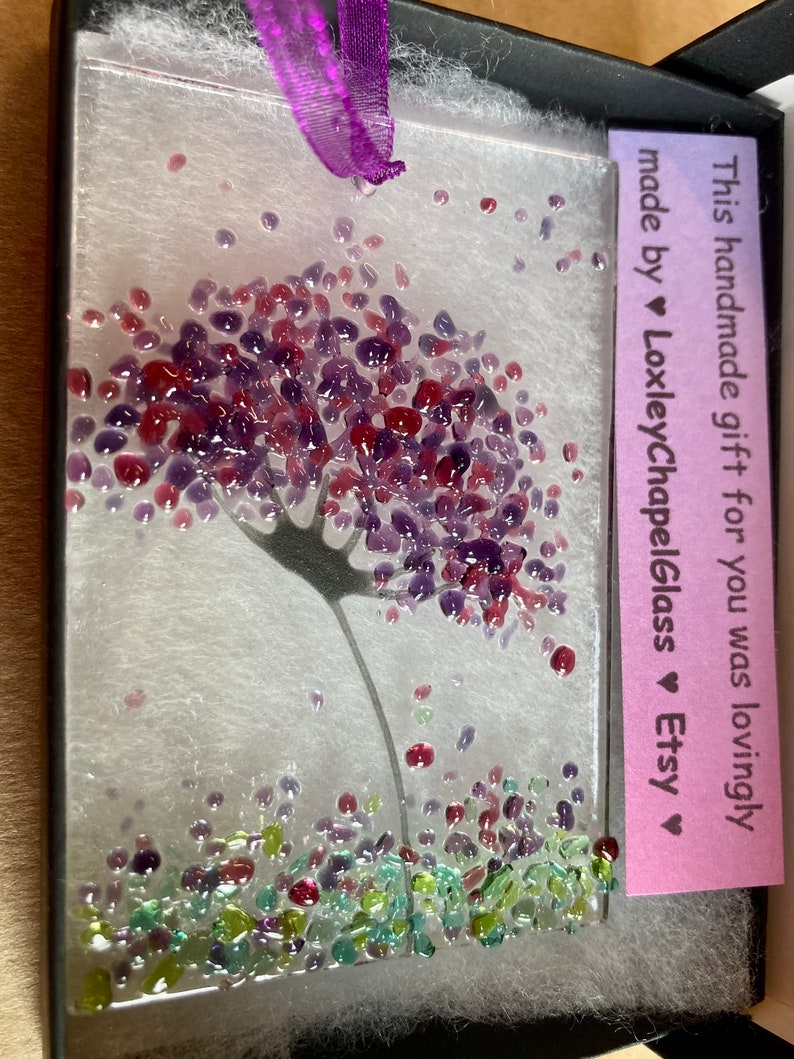 K&ouml;nnte beinhalten: Ein handgemachtes Glaskunstwerk mit einer lila Blume mit gr&uuml;nen und lila Glasakzenten. Das St&uuml;ck ist in einer schwarzen Box mit einer rosa Karte gerahmt, auf der steht: "Dieses handgemachte Geschenk f&uuml;r dich wurde liebevoll hergestellt von &hearts; LoxleyChapelGlass &hearts; Etsy &hearts;".