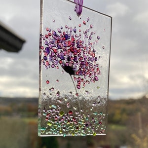 K&ouml;nnte beinhalten: Ein Glasornament mit einer lila und pinkfarbenen Blume mit einem gr&uuml;nen Stiel. Die Blume besteht aus kleinen Glassplittern und ist von kleineren gr&uuml;nen, lila und pinkfarbenen Glassplittern umgeben.
