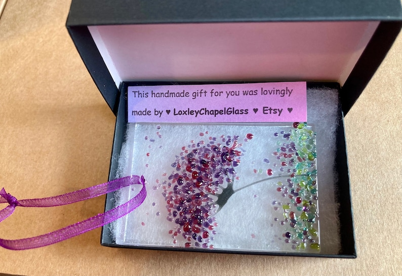 K&ouml;nnte beinhalten: Ein Glaskunstwerk mit einem lila und gr&uuml;nen Blumendesign in einer schwarzen Geschenkbox mit einem lila Band. Die Box enth&auml;lt eine Karte mit der Aufschrift "Dieses handgemachte Geschenk f&uuml;r dich wurde liebevoll hergestellt von &hearts; LoxleyChapelGlass &hearts; Etsy &hearts;".