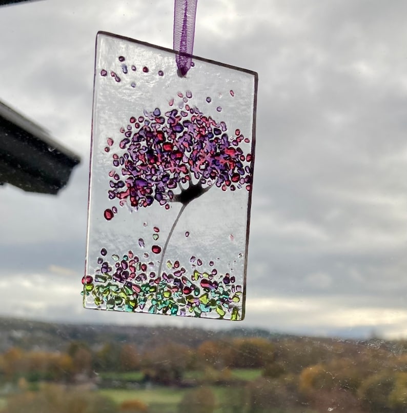 K&ouml;nnte beinhalten: Ein Glasornament mit einer lila und pinkfarbenen Blume mit einem langen Stiel und gr&uuml;nem und blauem Glitzer drumherum.