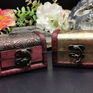 Op de afbeelding: Twee kleine houten schatkisten met sierlijke ontwerpen. De ene kist is rood met gouden accenten en de andere is goud met rode accenten. Beide kisten hebben een metalen sluiting.