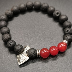 May include: A black lava rock beaded bracelet with a silver charm and red carnelian beads.