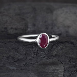 Può includere: Un anello d'argento con una pietra ovale di colore rosso intenso incastonata in una montatura a castone.