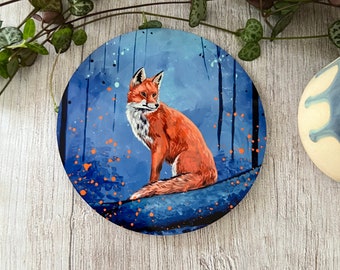Puede incluir: Un posavasos redondo pintado en azul y naranja con un zorro rojo sentado en una rama en un entorno de bosque.