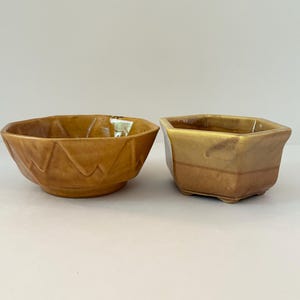 May include: A pair of glazed ceramic vessels in shades of golden brown. The left piece is a wide, shallow bowl with a faceted, zigzag-patterned exterior. The right piece is a hexagonal planter with a smooth, tapered body and small feet at the base.