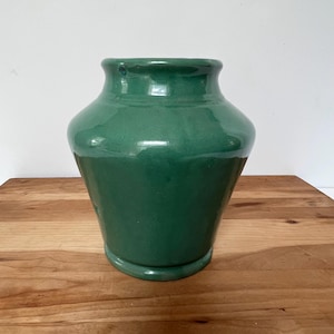 May include: A green ceramic vase with a rounded body and a flared lip. The vase has a smooth, glossy finish.