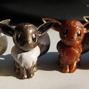 May include: Four small, detailed figurines of a Pokemon character. The figurines are in various shades of brown, gold, and white.
