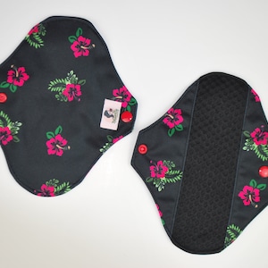 May include: Two black reusable cloth pads with a floral print of pink hibiscus flowers and green leaves. The pads have red snaps on the sides.