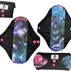 Puede incluir: Tres compresas menstruales de tela reutilizables con estampado de galaxia. Las compresas son negras con un estampado de galaxia colorido en el centro. Las compresas tienen broches de presión rosas y azules.