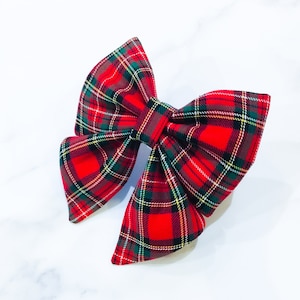 May include: A red, green, and brown plaid bow. The bow is made of fabric and has a classic bow shape.