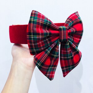 May include: Red velvet headband with a large plaid bow. The bow is made of red, green, and yellow plaid fabric.