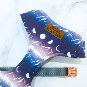 May include: A purple and white dog harness with a mountain and moon pattern. The harness has a brown leather tag that says "SARAH FUREVER".
