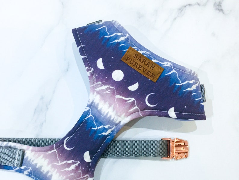 May include: A purple and white dog harness with a mountain and moon pattern. The harness has a brown leather tag that says "SARAH FUREVER".