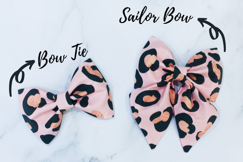 May include: Two pink and black leopard print fabric bows. The smaller bow is a bow tie and the larger bow is a sailor bow.