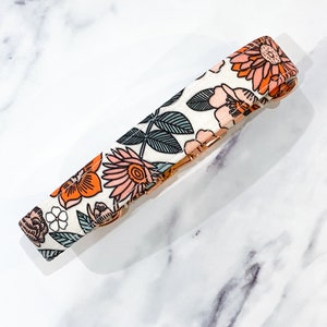 May include: A white dog collar with a floral pattern featuring orange, pink, and green flowers. The collar has a gold metal buckle.