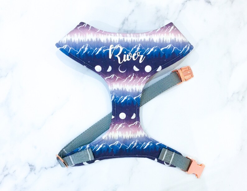 May include: A purple, blue, and white dog harness with a mountain and moon pattern. The harness has a rose gold buckle and the name "River" is printed on the front.