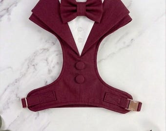 Puede incluir: Un arnés para mascota de color burdeos diseñado para parecer un esmoquin formal. Presenta una pajarita burdeos a juego en el cuello, una inserción de camisa blanca con dos botones pequeños y dos botones decorativos más grandes en el pecho.