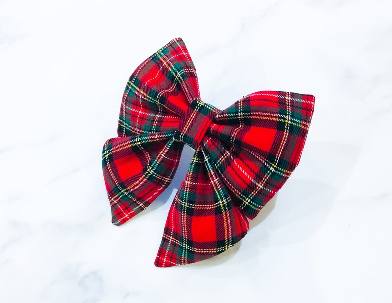 May include: A red, green, and brown plaid bow. The bow is made of fabric and has a classic bow shape.