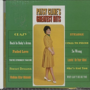 May include: CD case for Patsy Cline's Greatest Hits album. The cover features a photo of Patsy Cline in a yellow dress, with song titles listed on the sides. The album art has a green and yellow color scheme.