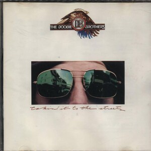 May include: A vintage album cover featuring a close-up of a person wearing sunglasses. The album cover is white with the text "THE DOOBIE BROTHERS" and "Takin' It to the Streets" in red.