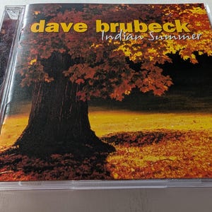 May include: CD case for Dave Brubeck's "Indian Summer" album. The cover shows a large tree with a thick trunk and a canopy of autumn leaves. The album title and artist's name are in gold lettering. The Telarc Jazz logo is in the bottom right corner.