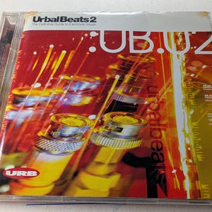 May include: A CD case for "Urbal Beats 2: The Definitive Guide to Electronic Music." The cover is red with yellow and orange abstract designs and the text "UB.02" in large white letters. The CD case is in a clear plastic case.