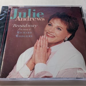 May include: A CD case featuring Julie Andrews, with the title "Broadway" and "The music of Richard Rodgers." The cover has a portrait of Julie Andrews in a white top, with the Philips logo in the bottom right corner.