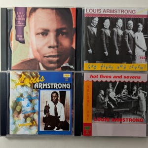 Puede incluir: Cuatro estuches de CD con música jazz. El estuche superior izquierdo tiene un retrato de un hombre y el texto "Bill 'Jazz' Gillum, The Bluebird Recordings 1934-1938". Los otros presentan a Louis Armstrong y el texto "Hot Fives and Sevens."
