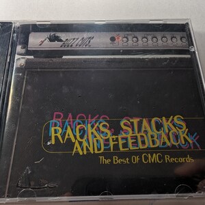 May include: A CD case with the album title "Racks, Stacks and Feedback: The Best of CMC Records" in colorful text. The cover features a graphic of a vintage amplifier with the text "Buzz Cuts" at the top.