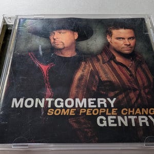 Op de afbeelding: CD-hoesje met de albumhoes van "Some People Change" van Montgomery Gentry. De cover toont twee mannen tegen een donkere achtergrond. Eén man draagt een zwarte cowboyhoed en een shirt met rode details. De andere draagt een gestreept bruin overhemd.
