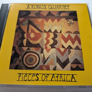 May include: A CD case with a yellow cover featuring the text "Kronos Quartet" and "Pieces of Africa." The cover art displays a geometric pattern in shades of brown, orange, and gold, set against a yellow background.