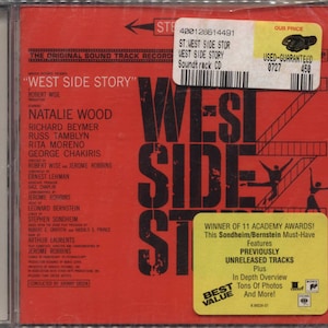 May include: A CD case for the "West Side Story" soundtrack. The cover is red with the title in large, bold, black letters. The names of the stars, including Natalie Wood, are listed. A sticker indicates the CD is used and guaranteed.