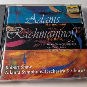 May include: A CD case with the album "Harmonium" by John Adams and "The Bells" by Sergei Rachmaninoff. The cover displays a colourful abstract design with text including the composers' names, performers, and the Atlanta Symphony Orchestra & Chorus.