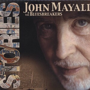 May include: Album cover for "Stories" by John Mayall & The Bluesbreakers. The cover features a close-up of a man's face with the band's name in white text. The word "STORIES" is vertically stacked on the left side, with comic book-style lettering.